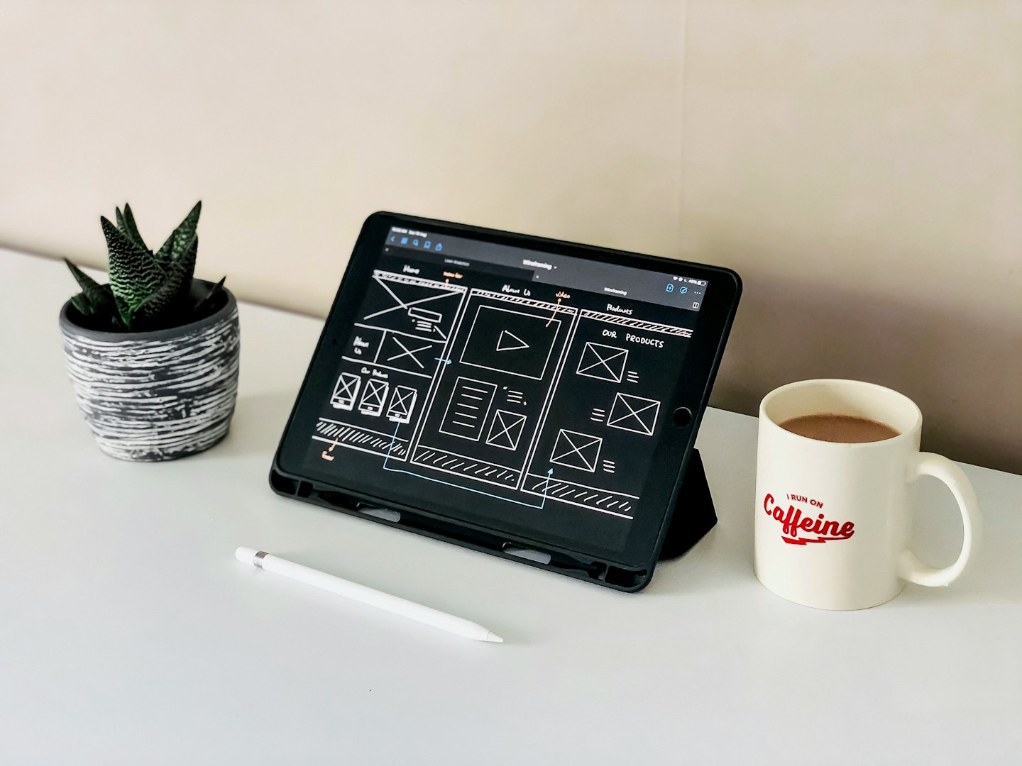 iPad with website wireframe, Apple Pencil, and coffee on a white desk.